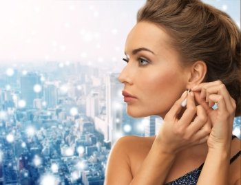 people, holidays, christmas and glamour concept - close up of beautiful woman wearing earrings over snowy city background