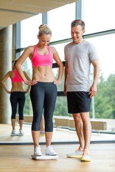 sport, fitness, lifestyle and people concept - smiling man and woman with scales in gym