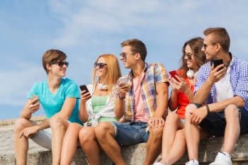 friendship, summer, technology and people concept - group of smiling friends with smartphones and headphones outdoors
