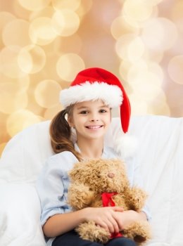 holidays, presents, christmas, childhood and people concept - smiling little girl with teddy bear toy over beige lights background