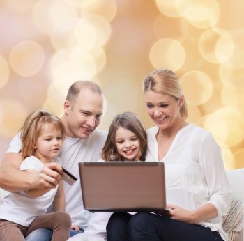 family, holidays, shopping, technology and people - happy family with laptop computer and credit card over beige lights background