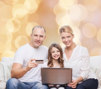 family, holidays, shopping, technology and people concept - happy family with laptop computer and credit card over beige lights background