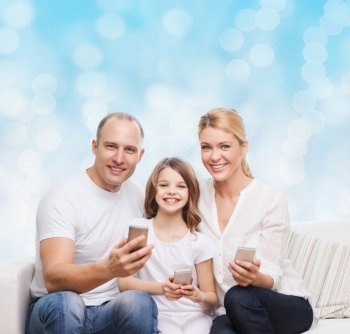 family, holidays, technology and people concept - smiling mother, father and little girl with smartphones over blue lights background