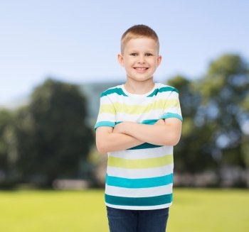 happiness, childhood, nature and people concept - smiling little boy in casual clothes with crossed arms over green park background