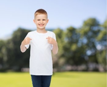 advertising, summer, people and childhood concept - smiling boy in white blank t-shirt pointing fingers at himself over park background