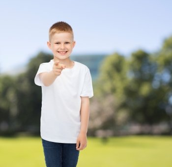 advertising, summer, gesture, people and childhood concept - smiling boy in white blank t-shirt pointing finger at you over park background