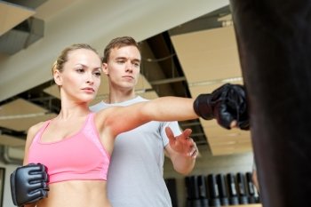 sport, fitness, lifestyle and people concept - woman with personal trainer boxing punching bag in gym