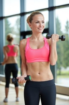 sport, fitness, training, weightlifting and people concept - young sporty woman with dumbbells flexing biceps in gym