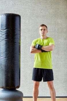 sport, box and people concept - young man with boxing gloves and punching bag in gym