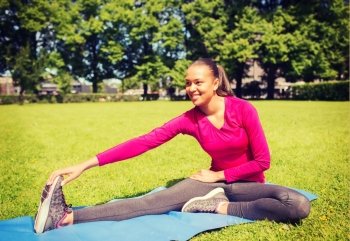 fitness, sport, training, park and lifestyle concept - smiling african american woman stretching leg on mat outdoors