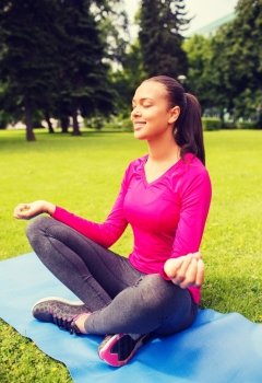 sport, meditation, park and lifestyle concept - smiling african american woman meditating on mat outdoors