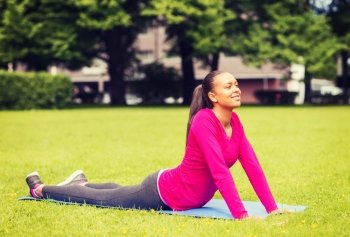 fitness, sport, training, park and lifestyle concept - smiling african american woman stretching on mat outdoors