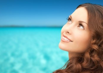 beauty, people and health concept - beautiful young woman looking up over blue sky and sea background