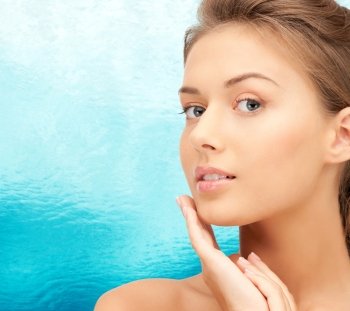 beauty, people and health concept - beautiful young woman touching her face over blue water background