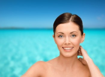 beauty, people and health concept - smiling young woman with bare shoulders over blue sky and sea background
