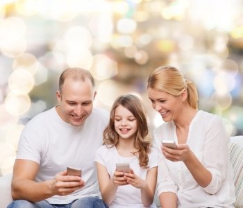 family, holidays, technology and people - smiling mother, father and little girl with smartphones over lights background