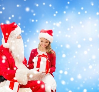 holidays, christmas, childhood and people concept - smiling little girl with santa claus and gifts over blue snowy background