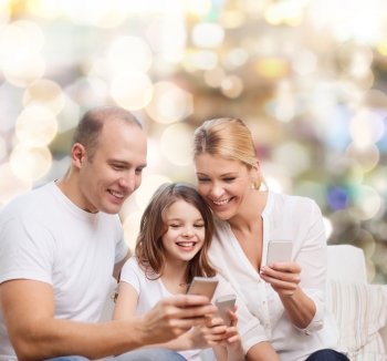 family, holidays, technology and people concept - smiling mother, father and little girl with smartphones over lights background