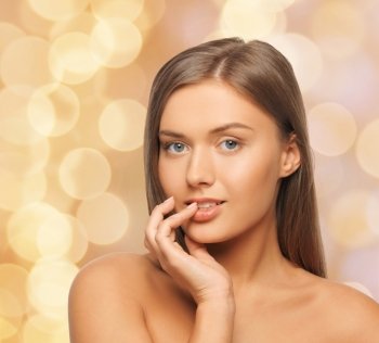 beauty, people and health concept - beautiful young woman touching her lips over beige lights background