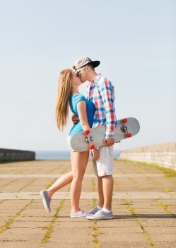 holidays, vacation and love concept - couple with skateboard kissing outdoors
