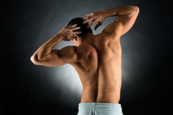 sport, bodybuilding, strength and people concept - young man standing over black background from back