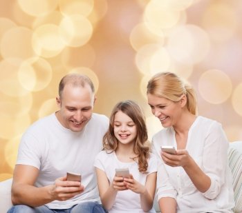 family, holidays, technology and people - smiling mother, father and little girl with smartphones over beige lights background