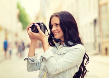 tourism, travel, leisure, holidays and friendship concept - smiling teenage girl with camera taking picture on street