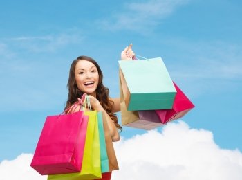 sale, gifts, holidays and people concept - smiling woman with colorful shopping bags over blue sky and white cloud background