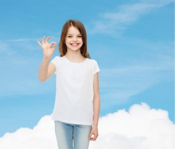 advertising, dream, gesture, childhood and people - smiling little girl in white blank t-shirt showing ok sign over blue sky background