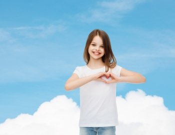 advertising, charity, childhood and people - smiling little girl in white blank t-shirt making heart-shape gesture over blue sky background