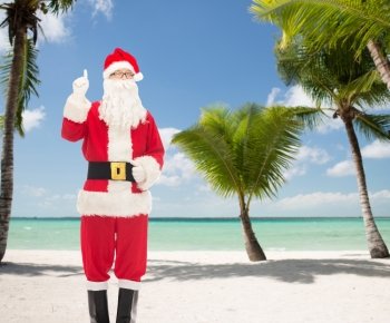 christmas, holidays, travel, gesture and people concept - man in costume of santa claus pointing finger up over tropical beach background