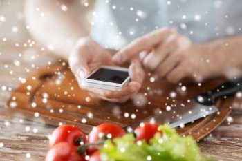 cooking, people, technology and home concept - closeup of man reading recipe from smartphone and vegetables on table in kitchen
