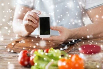 cooking, people, technology and home concept - closeup of man with vegetables on table showing blank smartphone screen in kitchen