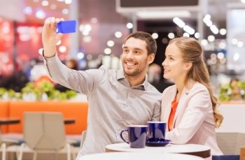 sale, shopping, consumerism, technology and people concept - happy young couple with smartphone taking selfie and drinking coffee or tea at cafe in mall