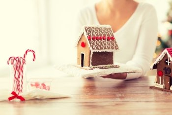 cooking, people, christmas and baking concept - close up of happy woman holding and showing gingerbread house at home