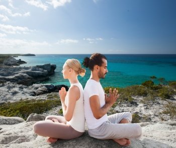 fitness, sport, yoga, people and lifestyle concept - happy couple sitting in lotus pose on beach