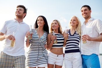 summer, holidays, tourism, drinks and people concept - group of smiling friends with bottles drinking beer or cider on beach