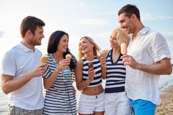 summer, holidays, sea, tourism and people concept - group of smiling friends eating ice cream and talking on beach