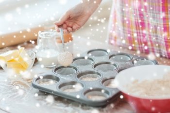 cooking, baking, food and home concept - close up of woman hand filling muffins molds with dough