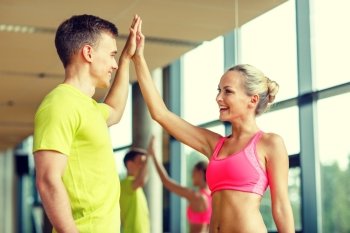 sport, fitness, lifestyle and people concept - smiling man and woman making high five in gym