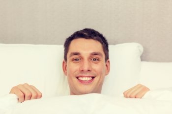 hotel, travel, relationships, and happiness concept - handsome man in bed