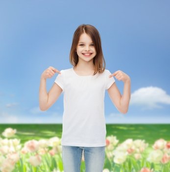 advertising, childhood, nature, gesture and people concept - smiling girl in white t-shirt pointing fingers on herself over field background