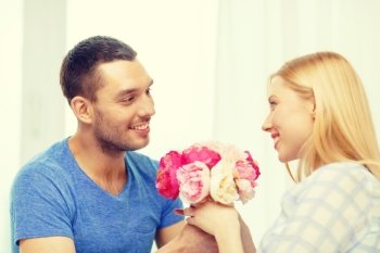 love, holiday, celebration and family concept - smiling man giving girfriens flowers at home
