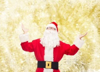 christmas, holidays and people concept - man in costume of santa claus with raised hands over yellow lights background