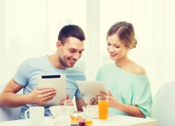 food, home, couple and technology concept - smiling couple with tablet pc reading news and having breakfast at home