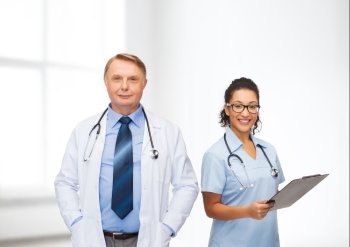 healthcare, profession and medicine concept - smiling doctors with clipboard and stethoscopes over clinic background