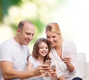 family, summer, technology and people concept - smiling mother, father and little girl with smartphones over green background