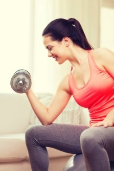 fitness, home and diet concept - smiling girl exercising with fitness ball and dumbbells at home