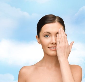 beauty, people and health concept - smiling young woman covering half of face with hand over blue sky background