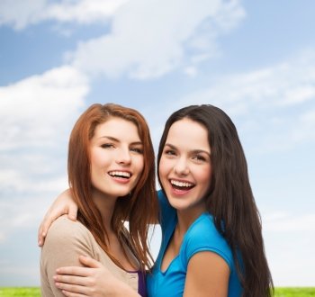 happiness, summer, friendship and people concept - smiling teenage girls hugging over blue sky and cloud background